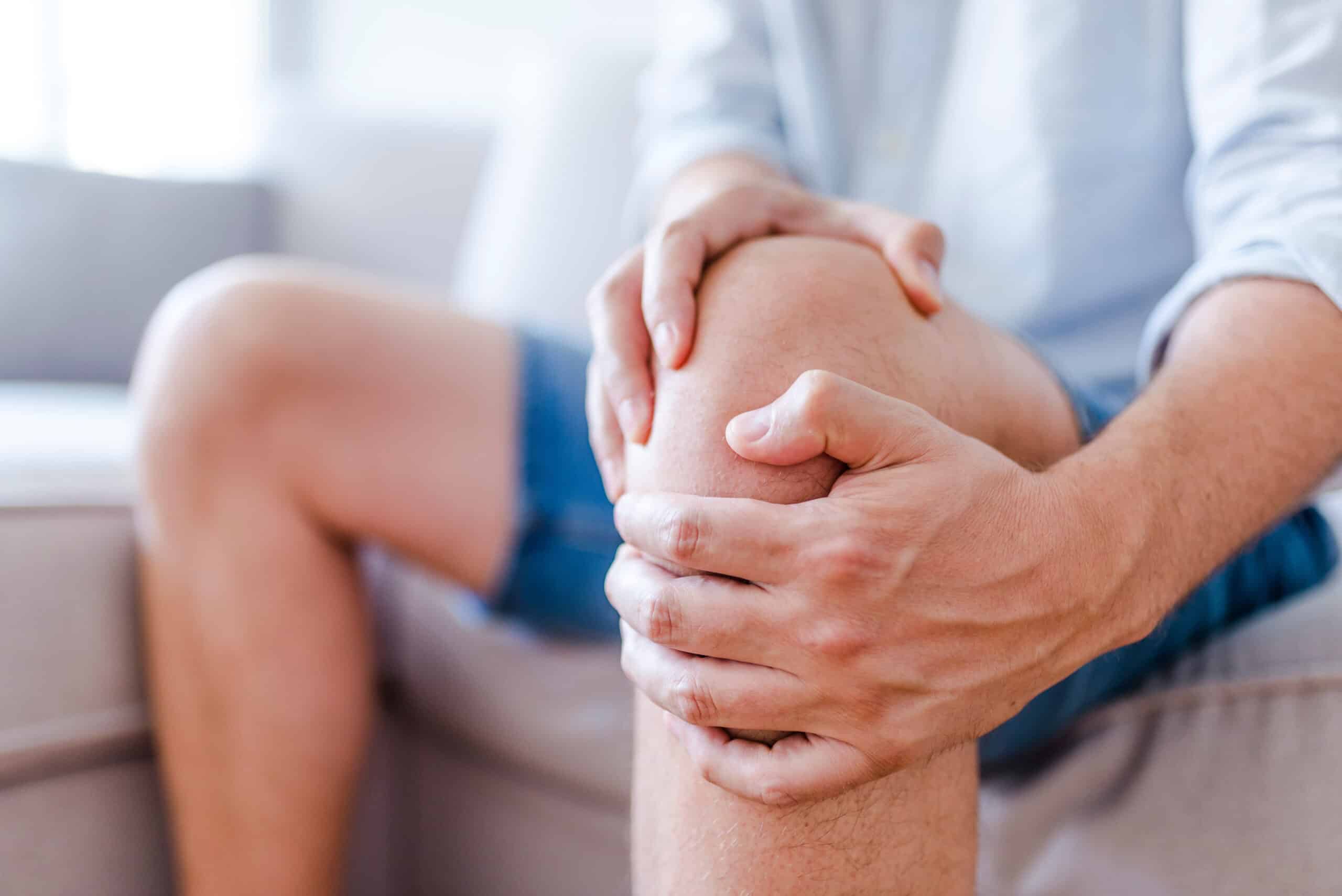 Man Suffering From Knee Pain Sitting On Sofa
